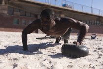 African american man exercising with weights on beach on sunny day. healthy outdoor lifestyle fitness training. — Photo de stock
