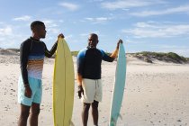 Afroamerikanischer Vater und Sohn mit Surfbrettern am Strand. Sommer-Strandurlaub und Freizeitkonzept. — Stockfoto