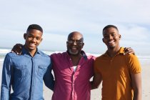 Retrato del padre afroamericano y sus dos hijos sonriendo mientras estaban juntos en la playa. vacaciones de playa de verano y concepto de ocio. - foto de stock