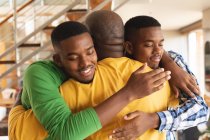 Hombre mayor afroamericano y sus dos hijos abrazándose en casa. paternidad y concepto familiar - foto de stock