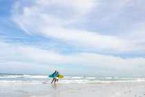Padre e hijo afroamericanos con tablas de surf caminando hacia la playa. vacaciones de playa de verano y concepto de ocio. - foto de stock