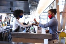 Diverse männliche und weibliche Kellner tragen Gesichtsmasken und benutzen Zahlungsterminals im Café. Unabhängiges Café, Geschäfte während der Coronavirus-Pandemie 19. — Stockfoto