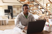 Joven afroamericano con auriculares usando portátil mientras estudia en casa. aprendizaje a distancia y concepto de educación en línea - foto de stock