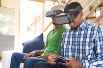 I fratelli afroamericani indossano cuffie vr giocando ai videogiochi mentre sono seduti sul divano di casa. concetto di tecnologia di gioco e intrattenimento — Foto stock