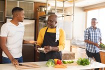 Un aîné afro-américain et ses deux fils cuisinent ensemble dans la cuisine à la maison. paternité et concept familial — Photo de stock