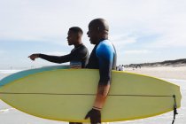 Padre e figlio afroamericano con tavole da surf che camminano verso le onde sulla spiaggia. estate vacanza al mare e concetto di svago. — Foto stock