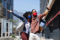 Homme de race mixte et femme afro-américaine portant des masques, embrassant, prenant selfie. traîner ensemble pendant une pandémie de coronavirus covid 19. — Photo de stock