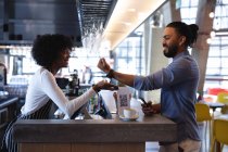 Smiling mixed race male client paying with smartwatch to african american female barista. independent cafe, small successful business. — Stock Photo