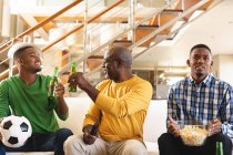 Uomo anziano afroamericano e i suoi due figli che guardano sport insieme in TV a casa. famiglia, sport e divertimento concetto — Foto stock