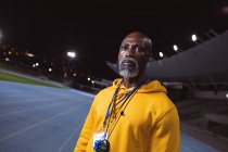 Entraîneur senior afro-américain debout sur la piste de course la nuit. concept de sport paralympique — Photo de stock