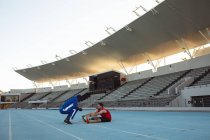 Treinador masculino afro-americano instruindo atleta masculino caucasiano com perna protética na pista de corrida. conceito de esporte paralímpico — Fotografia de Stock
