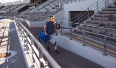 Кавказский спортсмен с протезной ногой в маске для лица ходит по стадиону. паралимпийский спорт и концепция эпидемии ковида-19 — стоковое фото