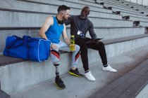 Treinador masculino afro-americano apoiando atleta masculino caucasiano com perna protética no estádio. conceito de esporte paralímpico — Fotografia de Stock