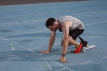 Atleta masculino caucasiano com perna protética em posição inicial para corrida na pista. conceito de esporte paralímpico — Fotografia de Stock