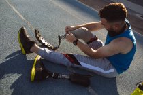 Atleta masculino caucasiano consertando sua perna protética enquanto estava sentado na pista de corrida no estádio. conceito de esporte paralímpico — Fotografia de Stock