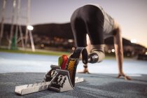 Caucasian male athlete with prosthetic leg in starting position for running on the track at night. paralympic sport concept — Stock Photo