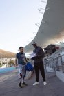 Entrenador masculino afroamericano instruyendo a atleta masculino caucásico con pierna protésica en el estadio. concepto de deporte paralímpico - foto de stock