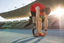 Caucasian male athlete with prosthetic leg performing stretching exercise on running track. paralympic sport concept — Stock Photo
