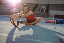 Atleta masculino caucasiano com perna protética realizando exercício de alongamento em pista de corrida. conceito de esporte paralímpico — Fotografia de Stock