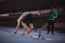Atleta maschio caucasico con gamba protesica in posizione di partenza per correre in pista di notte. concetto di sport paralimpico — Foto stock