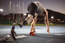 Caucasian male athlete with prosthetic leg in starting position for running on the track at night. paralympic sport concept — Stock Photo