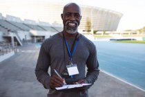 Retrato do treinador americano africano segurando prancheta sorrindo enquanto estava no estádio. conceito de esporte paralímpico — Fotografia de Stock