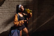 Fit afrikanisch-amerikanische Frau mit Turnbeutel Trinkwasser steht gegen Backsteinmauer in der Stadt. gesunder urbaner aktiver Lebensstil und Outdoor-Fitness. — Stockfoto