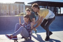 Trois heureuses amies caucasiennes et masculines jouant avec le skateboard au soleil. traîner dans un skatepark urbain en été. — Photo de stock