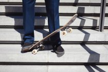Низкая часть бизнесмена, стоящего на скейтборде под солнцем. тусоваться в городском скейтпарке летом. — стоковое фото