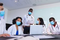 Команда різноманітних лікарів, які носять маску для обличчя, обговорює разом ноутбук у залі засідань. охорона здоров'я та медичні дослідження під час прихованої пандемії 19 — стокове фото