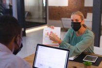 Kaukasische Bürokollegen mit Gesichtsmasken diskutieren im Büro über ein Dokument. Hygiene und soziale Distanzierung am Arbeitsplatz während der covid-19-Pandemie. — Stockfoto