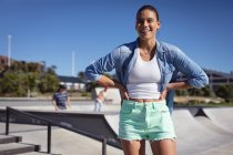 Mujer caucásica feliz de pie y sonriendo a la cámara. pasando el rato en skatepark urbano en verano. - foto de stock