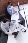 Vue aérienne de l'homme afro-américain portant un masque facial parlant sur smartphone tout en utilisant un ordinateur portable. hygiène et distanciation sociale sur le lieu de travail lors d'une pandémie de coqueluche 19. — Photo de stock