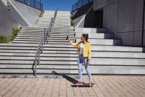 Lächelnde Kaukasierin, die auf dem Skateboard steht und neben der Treppe ein Selfie macht. Abhängen im städtischen Skatepark im Sommer. — Stockfoto