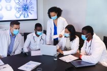 Team verschiedener Ärzte mit Gesichtsmaske diskutieren gemeinsam bei Laptop im Besprechungsraum. Gesundheitswesen und medizinische Forschung während der covid 19 Pandemie — Stockfoto