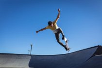 Hombre caucásico saltando y patinando en un día soleado. pasando el rato en skatepark urbano en verano. - foto de stock