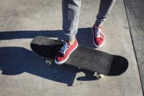 Sección baja de la mujer de pie en el monopatín en el sol. pasando el rato en un skatepark urbano en verano. - foto de stock