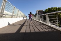Fit afrikanisch-amerikanische Frau läuft auf Fußgängerbrücke und trainiert in der Stadt. gesunder aktiver Lebensstil und Outdoor-Fitness. — Stockfoto