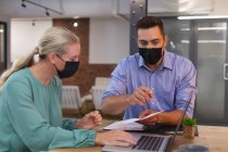 Kaukasische Bürokollegen mit Gesichtsmasken diskutieren im Büro über ein Dokument. Hygiene und soziale Distanzierung am Arbeitsplatz während der covid-19-Pandemie. — Stockfoto