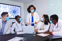 Team of diverse doctors wearing face mask discussing together over laptop in the meeting room. healthcare and medical research during covid 19 pandemic — Stock Photo