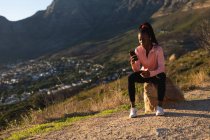 Donna afroamericana che si prende una pausa in esercizio all'aperto, indossando auricolari e utilizzando smartphone. sano stile di vita attivo e fitness all'aperto. — Foto stock