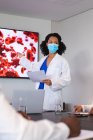 Afrikanisch-amerikanische Ärztin mit Gesichtsmaske bei der Präsentation vor einem Ärzteteam. Gesundheitswesen und medizinische Forschung während der covid 19 Pandemie — Stockfoto