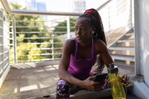 Жирна афро-американська жінка сидить на сходинках з навушниками, використовуючи смартфон під час тренувань у місті. Здоровий міський активний спосіб життя і зовнішній вигляд. — стокове фото