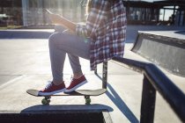 Niedriger Abschnitt einer kaukasischen Frau, die mit dem Skateboard auf einem Geländer in der Sonne sitzt. Im Sommer im städtischen Skatepark abhängen. — Stockfoto