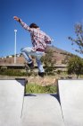 Visão traseira do homem caucasiano pulando e skate no dia ensolarado. sair no parque de skate urbano no verão. — Fotografia de Stock