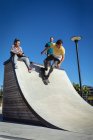 Three happy caucasian female and male friends skateboarding in the sun. hanging out at an urban skatepark in summer. — Stock Photo