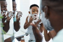 Африканський американський батько і син у ванній кімнаті, застосовуючи піну для гоління. вдома в ізоляції під час карантину.. — стокове фото