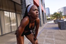 Ajuste mujer afroamericana tomando un descanso durante el ejercicio en la ciudad. estilo de vida activo urbano saludable y fitness al aire libre. - foto de stock