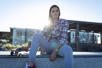 Portrait de femme caucasienne assise sur un mur avec planche à roulettes au soleil. traîner dans un skatepark urbain en été. — Photo de stock