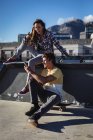 Щаслива біла жінка і чоловік сидять на стіні зі скейтбордами, використовуючи смартфон на сонці. висить у міському скейтпарку влітку . — стокове фото
